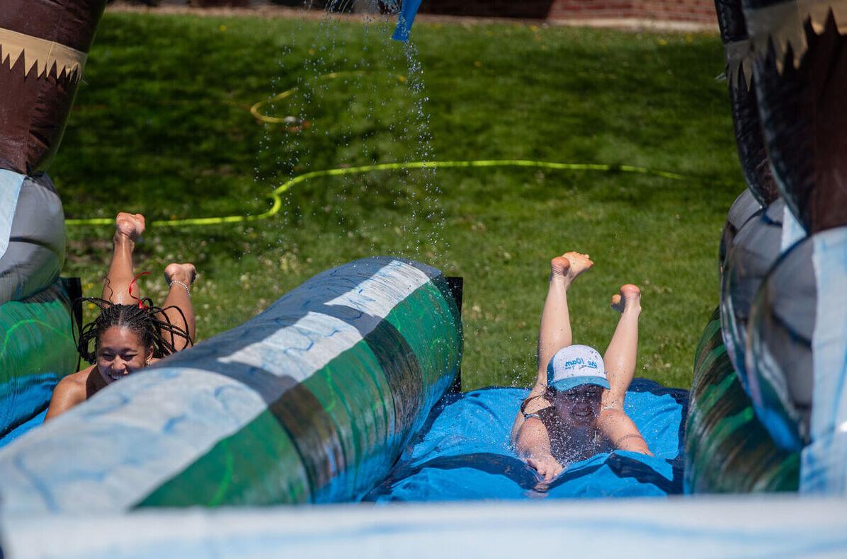 Two female students dive down a water slide during May Day