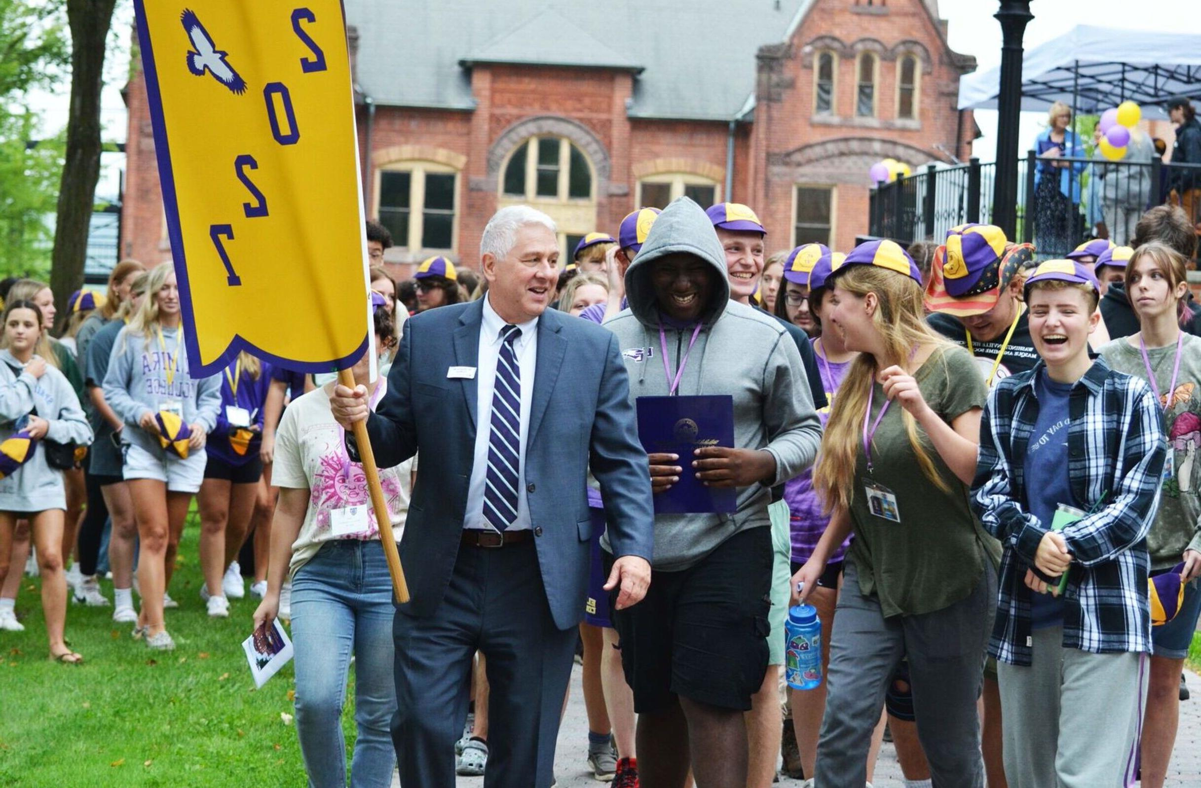 President Charles 林赛 holds a 2027 flag as he leads a procession of new students following the fall welcome.